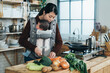 © PR Image Factory - asian new mother is using a knife to cut vegetables with her newborn baby in the carrier in a modern bright kitchen at home.