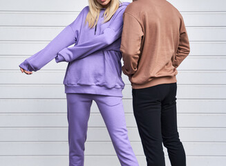 Blonde girl is standing in blue sport outfit. Man wears brown hoodie and black pants. Couple is wearing street matching outfit