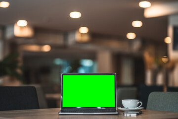 Wall Mural - Mockup of laptop computer with empty screen with coffee cup and smartphone on table of the coffee shop background,Green screen