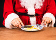 © Sinica Kover - Christmas healthy breakfast of Santa. Close up of Santa Claus's hands in traditional red costume with knife and fork slicing scrambled eggs.