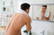 © New Africa - Handsome man touching his smooth face after shaving near mirror in bathroom