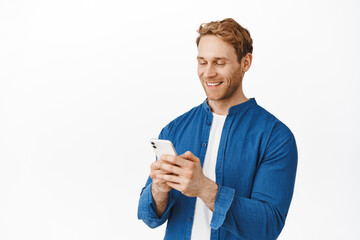 Modern candid guy with phone in hands chatting, message or read screen, smiling at smartphone display while using application, standing over white background