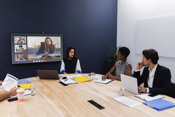 Diverse group of business colleagues having video call with coworkers on screen in meeting room