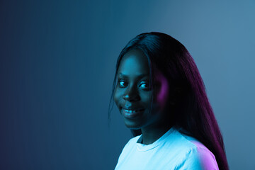 Wall Mural - Portrait of young African beautiful girl isolated over dark background in mixed neon light.