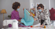 © TommyStockProject - Team of fashion designer wearing safety mask discussing sketch and choosing fabric in workshop