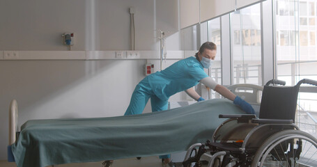 Portrait of female nurse wearing safety mask and gloves changing sheets in hospital.