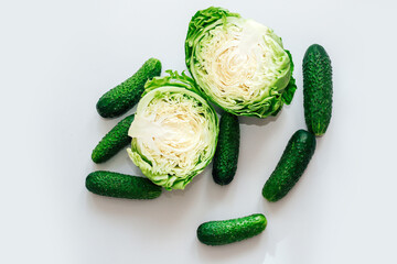 Wall Mural - Young cabbage cut in half with cucumbers top view on gray background.