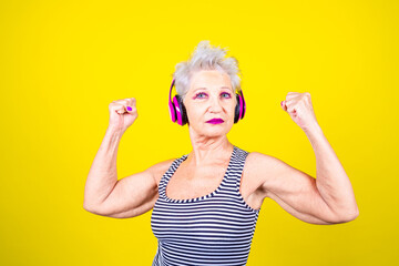 Wall Mural - Mature woman isolated background showing muscle powerful training using headphones