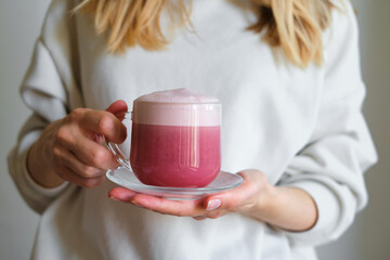 A cup of red velvet latte in the hands of a girl on a light background. Hot tasty drink. Trendy beetroot trendy drink with milk. A healthy alternative tasty dessert in a clear glass cup. Poster