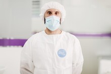 Positive Male Doctor With Latex Gloves And Protective Medical Mask With Covid-19 Vaccinated Message Sticker On White Uniform Standing In Modern Medical Office And Looking At Camera