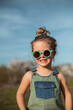 © Aizane/ADDICTIVE STOCK - Content little girl in overalls and sunglasses standing in meadow and enjoying summer on sunny day in countryside