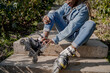© Alvaro Atalaya/ADDICTIVE STOCK - Smiling African American female putting on rollerblades while sitting on stairs in summer park and looking away