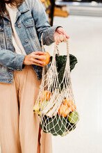 Cropped Unrecognizable Female Standing With Assorted Fruits And Vegetables In Eco Friendly Mesh Bag Against Blue Wall In City