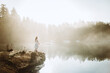 © Camille Girard/ADDICTIVE STOCK - Back view woman standing dressed in a white dress on a rock looking at a lake on a foggy day