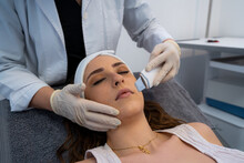 Crop Unrecognizable Cosmetologist Doing Ultrasonic Face Peeling For Relaxed Woman Lying On Medical Table In Modern Beauty Clinic