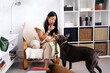 © Jake Jakab/ADDICTIVE STOCK - Ethnic female showing silence gesture while interacting with purebred dog and sitting in armchair at home