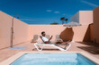 © Jairo Diaz/ADDICTIVE STOCK - Side view of male freelancer lying on lounger at poolside and surfing Internet on mobile phone during telework in summer on sunny day