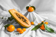 © Harry Rendon/ADDICTIVE STOCK - Half of pawpaw with seeds between tangerines and cumquats with leaves on white crumpled cloth
