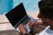 © Jairo Diaz/ADDICTIVE STOCK - Male freelancer lying on lounger at poolside and surfing Internet on laptop during telework in summer on sunny day