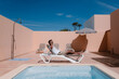 © Jairo Diaz/ADDICTIVE STOCK - Side view of male freelancer lying on lounger at poolside and speaking on mobile phone during telework in summer on sunny day