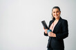 © Jake Jakab/ADDICTIVE STOCK - Positive middle aged female entrepreneur with ponytail wearing formal suit looking at camera while standing with folder and cup of drink on white background