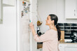© Jake Jakab/ADDICTIVE STOCK - Side view of positive middle aged female making notes in calendar on fridge while having phone call in modern kitchen