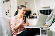 © Jake Jakab/ADDICTIVE STOCK - Side view of smiling middle aged female sitting on couch and showing picture of baby while having video chat on netbook on blurred background