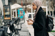 © Jake Jakab/ADDICTIVE STOCK - Side view of Muslim female in headscarf using bicycle sharing system in city