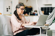 © Jake Jakab/ADDICTIVE STOCK - Side view full body of concentrated middle aged female in eyeglasses typing on netbook while sitting on sofa in room with kitchen on blurred background