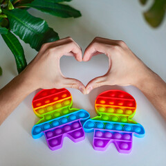 Hands of young man shaped as heart near two fidget sensory figures with lgbtq colorful rainbow flag, love and equality, gay pride concept