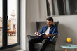 © Manuel Ruiz/ADDICTIVE STOCK - Concentrated young Hispanic guy in casual clothes sitting in comfortable armchair and reading interesting book near table with glass of fresh orange juice in daylight at home