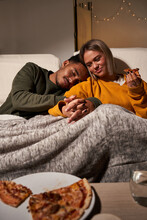 Multiethnic Couple Sitting In Sofa And Girlfriend Eating Delicious Pizza While Boyfriend Sleep