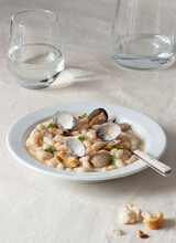 Appetizing Traditional Spanish Stewed White Fabes Beans With Mollusks In Plate With Fresh Parsley Leaves On Tablecloth