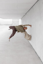 Male Dancer Balancing On Arm And Showing Breakdance Movement While Leaning On Concrete Wall Of Building In City