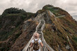 © Sergio Victor Vega/ADDICTIVE STOCK - Back view of unrecognizable male tourist with backpack and hat standing on wooden pathway in a cliff and admiring scenery of mountain views in seashore during summer vacation