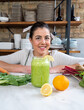 © The Trio Studio/ADDICTIVE STOCK - Cheerful female looking at camera at table with jar of delicious vegan smoothie and fresh citrus fruits in kitchen