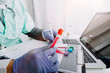 © ARMMY PICCA - doctor hand taking a blood sample tube from a rack with machines of analysis in the lab background