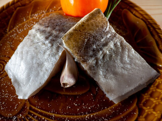 Wall Mural - Closeup shot of slightly salted raw fish fillets with green onion and tomato on a plate