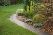 Backyard Garden Modern Design Landscaping. Decorative Garden Winding Pathway Walkway From Black Bricks. Back Yard Lawn And Natural Mulched Border Between Grass And Curved Brick Paving. Path To House.