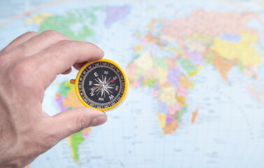 male hand showing compass on the world map background.