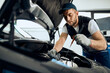 © Drazen - Young mechanic checking oil level of car engine at repair workshop.