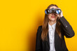 young business woman looking through binoculars on a yellow background