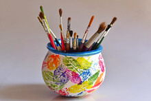 Artist's Painting Brushes In A Painted Pot, Against White Background.