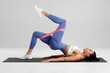 © nikolas_jkd - Fitness woman doing glute bridge exercise with resistance band on gray background. Athletic girl working out