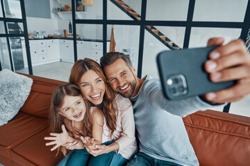 Wall Mural - Happy young family smiling and using smart phone to take a selfie 