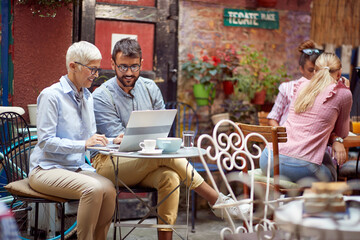 Wall Mural - An older woman and her young male friend watching a laptop content while sitting in a bar. Leisure, bar, outdoor, friendship