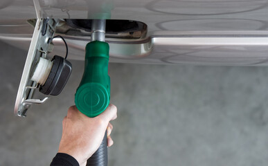 Wall Mural - Gas station worker filling up bronze pickup truck tank (Top View). Closeup hand holding green gas pump nozzle.