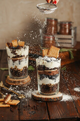 Wall Mural - Sifting powdered sugar over two glasses with a layered dessert trifle with chocolate, cream, cookies and blueberries