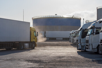 Canvas Print - Dirt parking for trucks with a large fuel tank in the background.