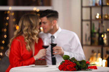 lovely couple celebrating valentine's day in restaurant, focus on table with red roses